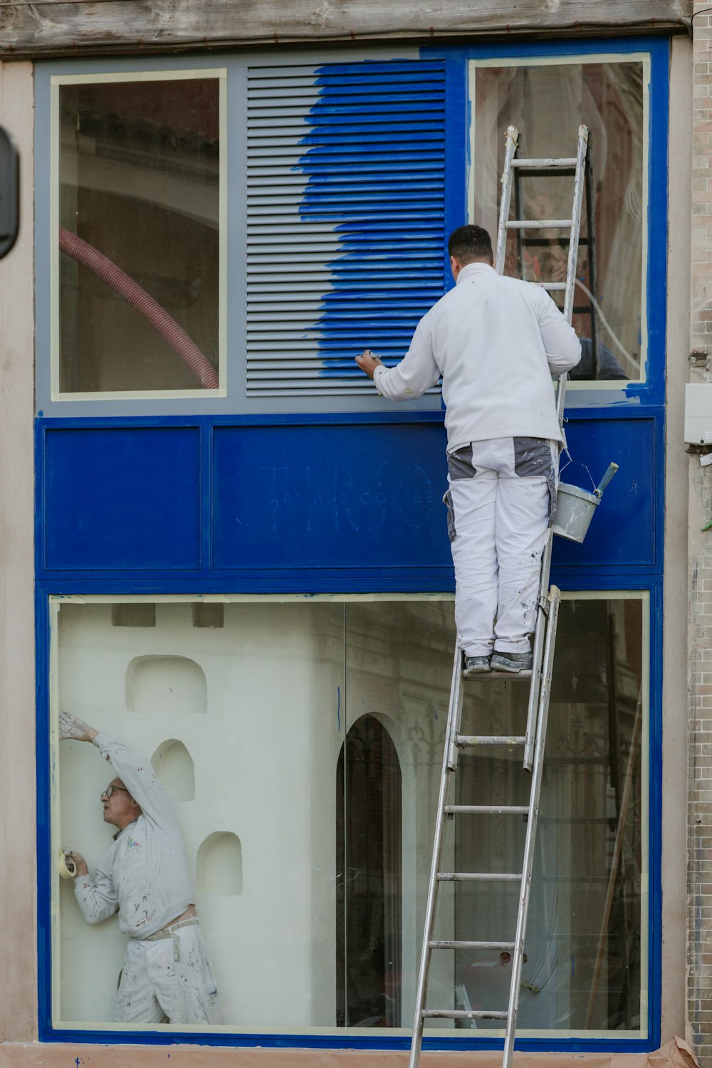 はしごで建物の窓枠を塗装する職人(イメージ写真)